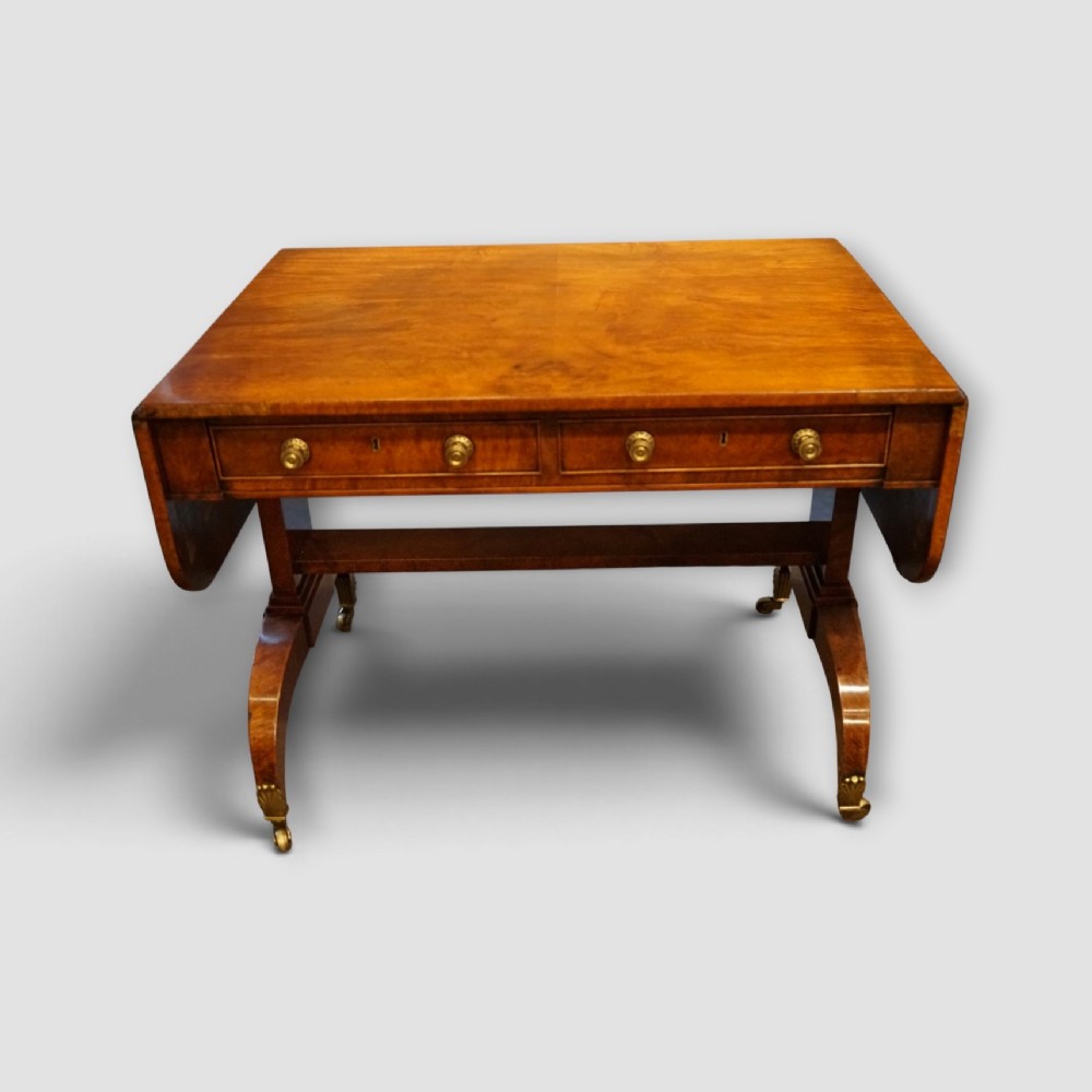 A Regency burr satinwood sofa table with drop leaves, two frieze drawers, brass handles, and splayed legs on castors. View VIII