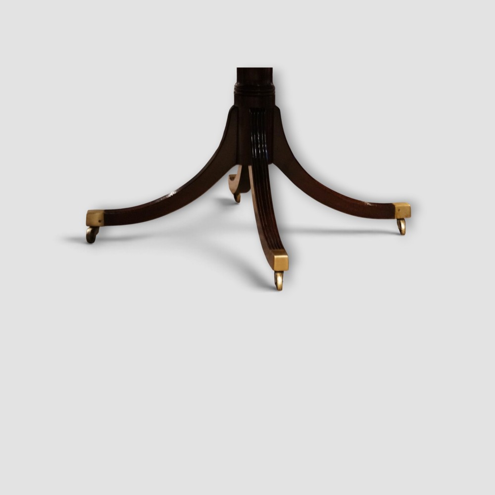 An extended mahogany twin pedestal dining table featuring a polished surface, rounded corners, reeded tripod legs, and brass castors. View VIII