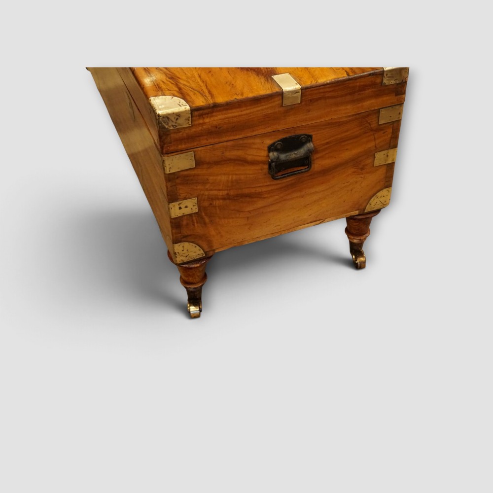 A low rectangular warm amber camphor wood campaign trunk featuring brass strap corners, flush brass handles, dual keyholes, and turned legs with castors. View III