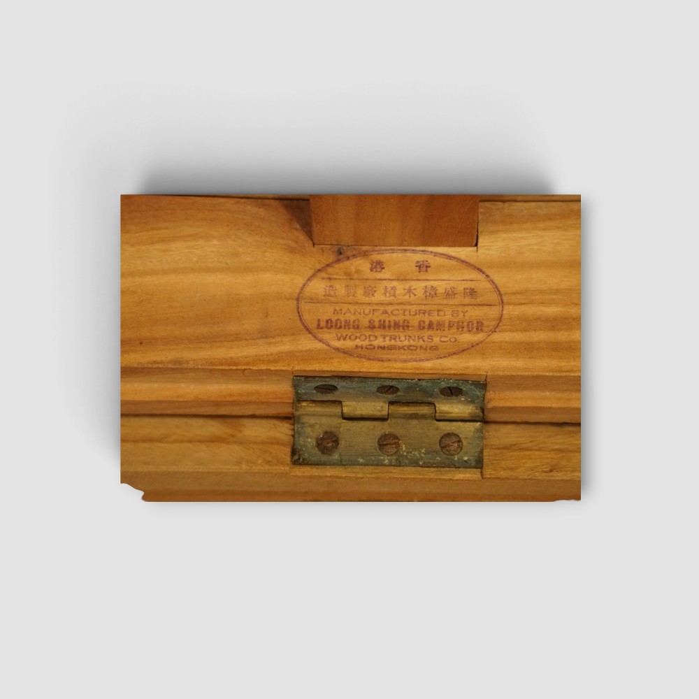 A low rectangular warm amber camphor wood campaign trunk featuring brass strap corners, flush brass handles, dual keyholes, and turned legs with castors. View X