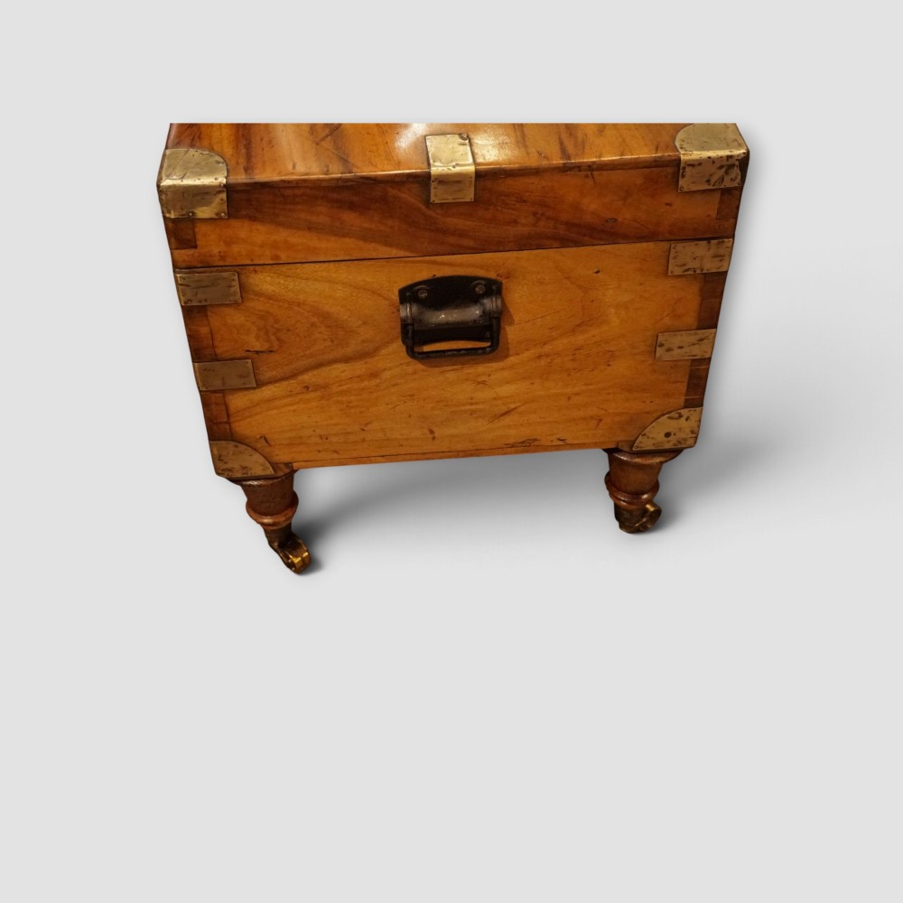 A low rectangular warm amber camphor wood campaign trunk featuring brass strap corners, flush brass handles, dual keyholes, and turned legs with castors. View XII