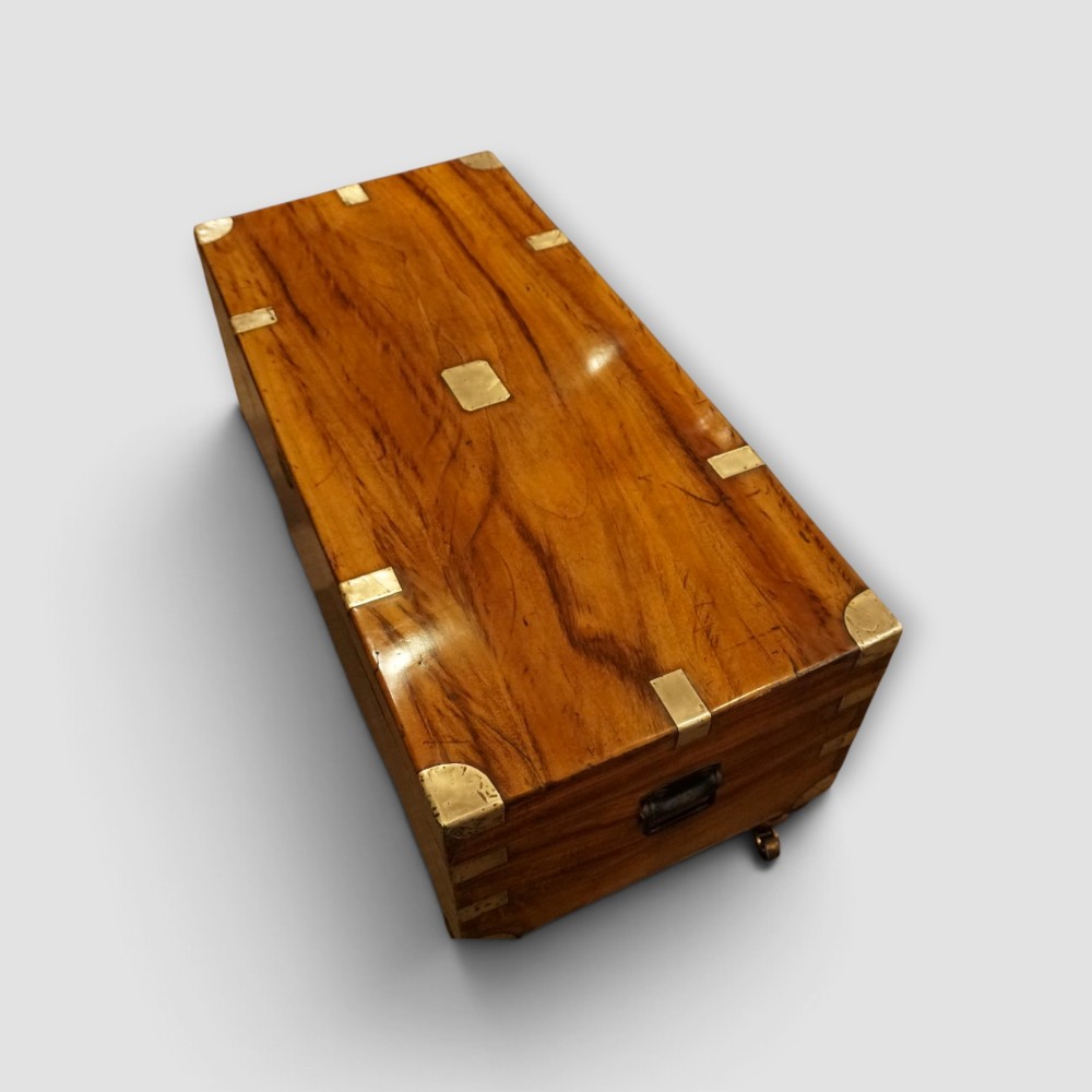 A low rectangular warm amber camphor wood campaign trunk featuring brass strap corners, flush brass handles, dual keyholes, and turned legs with castors. View XIII