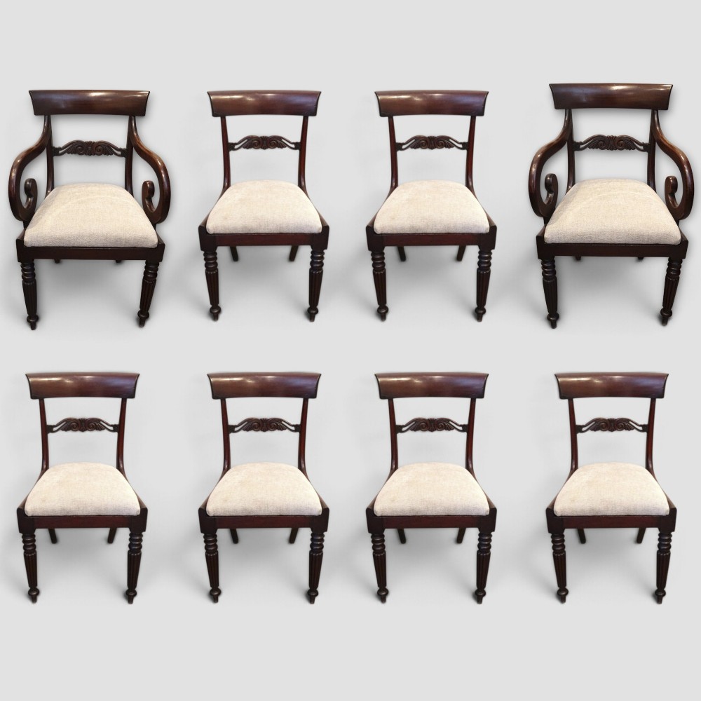 A set of eight William IV dark mahogany dining chairs comprising six side chairs and two carvers with turned front legs and light neutral upholstered seats.