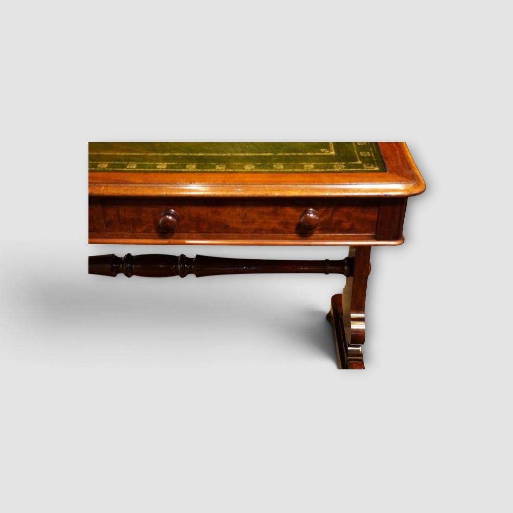 An early Victorian mahogany writing table featuring a green leather inset top with gilt tooling, two frieze drawers, a turned stretcher, and end supports. View IV