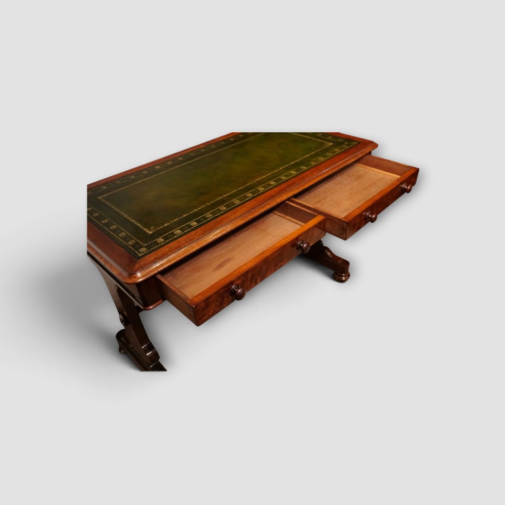 An early Victorian mahogany writing table featuring a green leather inset top with gilt tooling, two frieze drawers, a turned stretcher, and end supports. View V