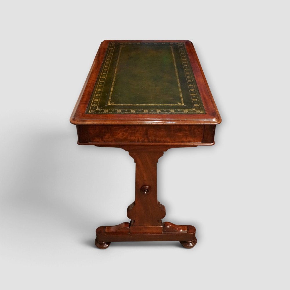 An early Victorian mahogany writing table featuring a green leather inset top with gilt tooling, two frieze drawers, a turned stretcher, and end supports. View VII