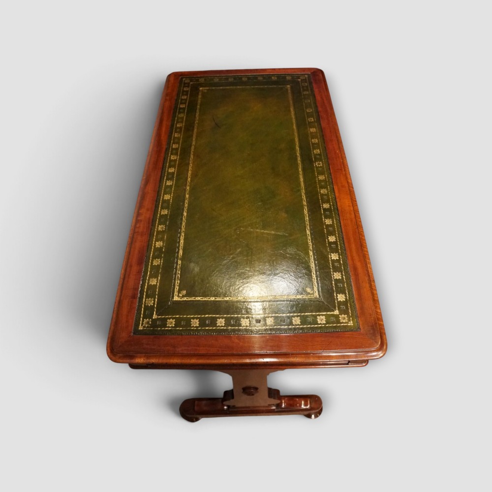 An early Victorian mahogany writing table featuring a green leather inset top with gilt tooling, two frieze drawers, a turned stretcher, and end supports. View IX