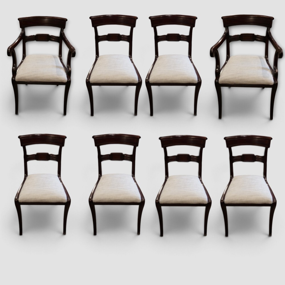 A set of eight Regency mahogany dining chairs with neutral cream upholstery, carved back rails, and curved sabre legs.