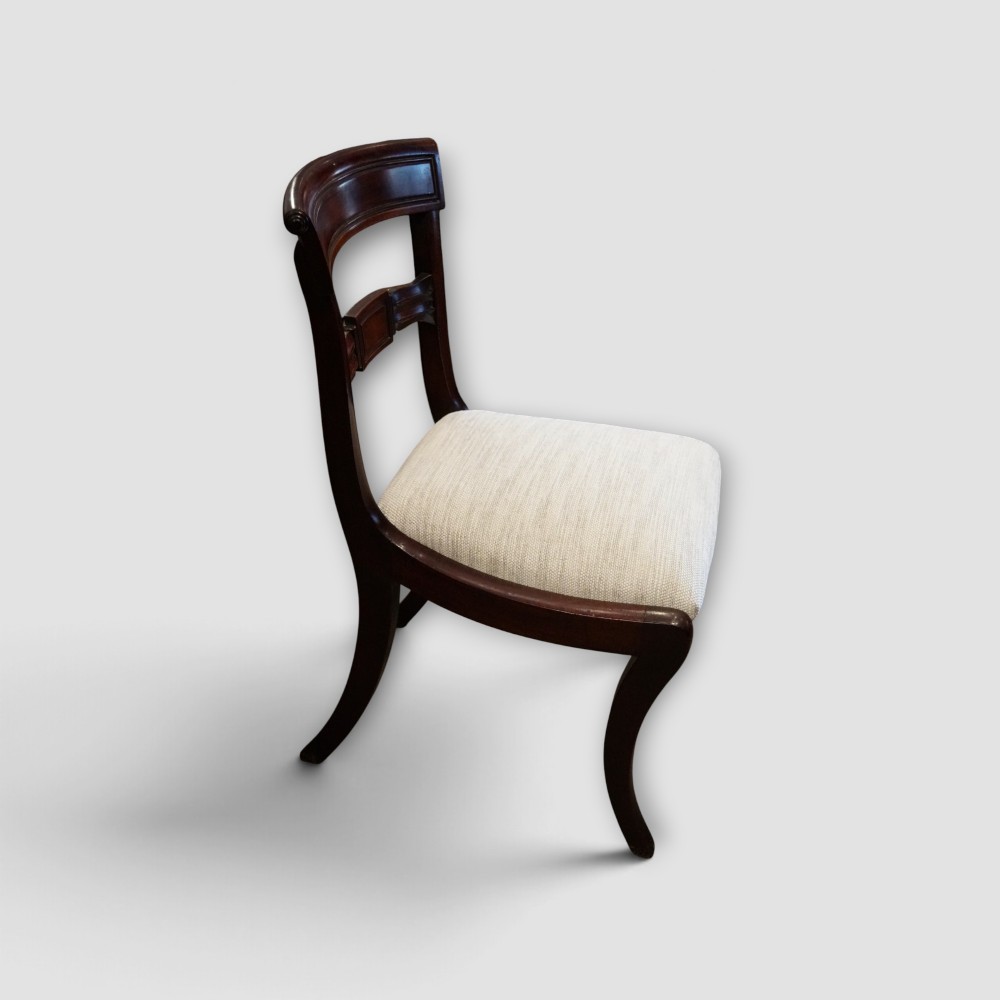 A set of eight Regency mahogany dining chairs with neutral cream upholstery, carved back rails, and curved sabre legs. View V