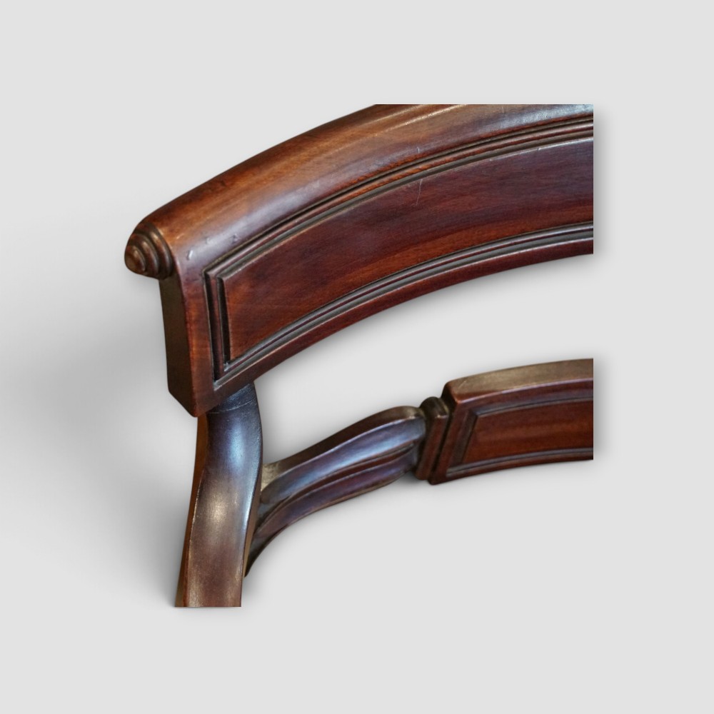 A set of eight Regency mahogany dining chairs with neutral cream upholstery, carved back rails, and curved sabre legs. View VII