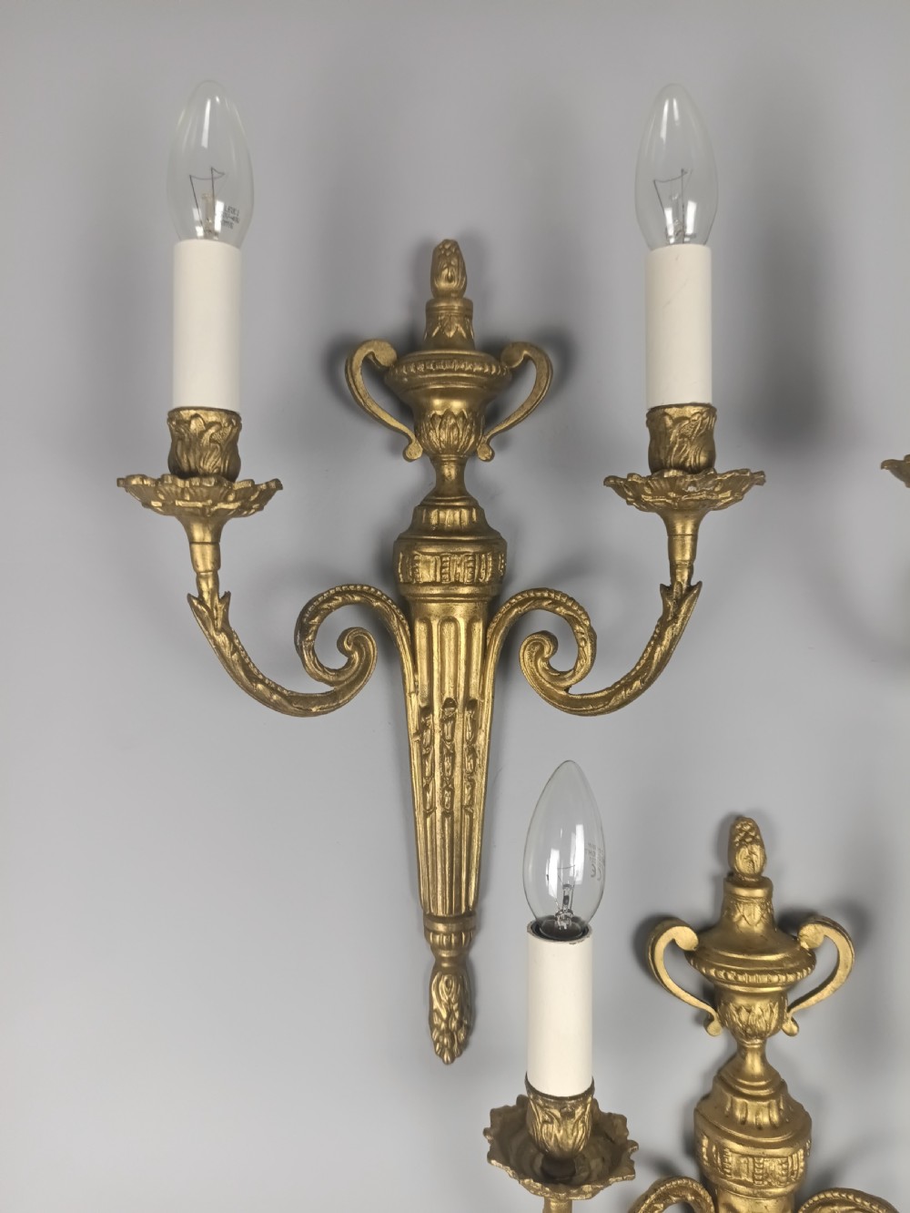 Set of three French gilded brass wall sconces featuring twin scrolling arms and urn-shaped tapered backplates. View III