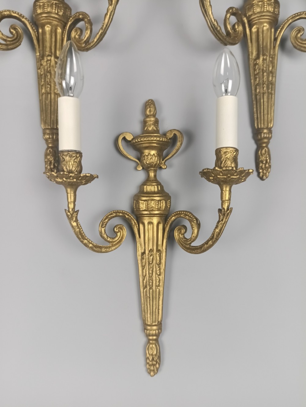 Set of three French gilded brass wall sconces featuring twin scrolling arms and urn-shaped tapered backplates. View IV