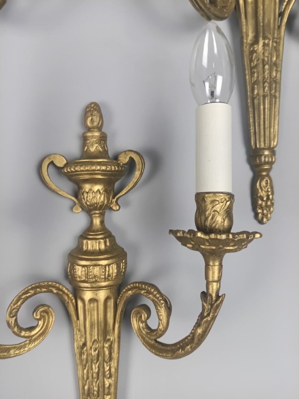 Set of three French gilded brass wall sconces featuring twin scrolling arms and urn-shaped tapered backplates. View V