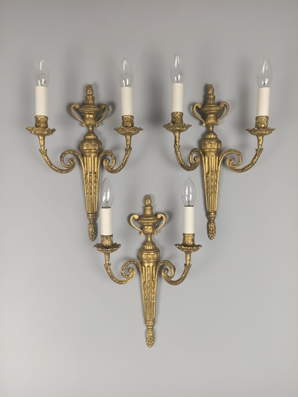 Set of three French gilded brass wall sconces featuring twin scrolling arms and urn-shaped tapered backplates. View VII