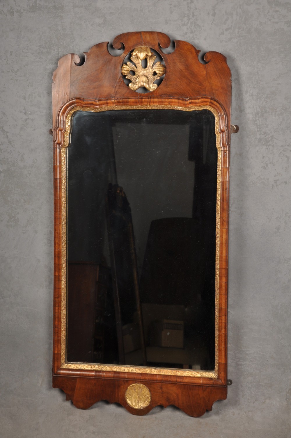 An early 18th-century walnut wall mirror featuring shaped scroll cresting with a carved giltwood shell motif and a gilded inner slip surrounding a rectangular mirror glass.