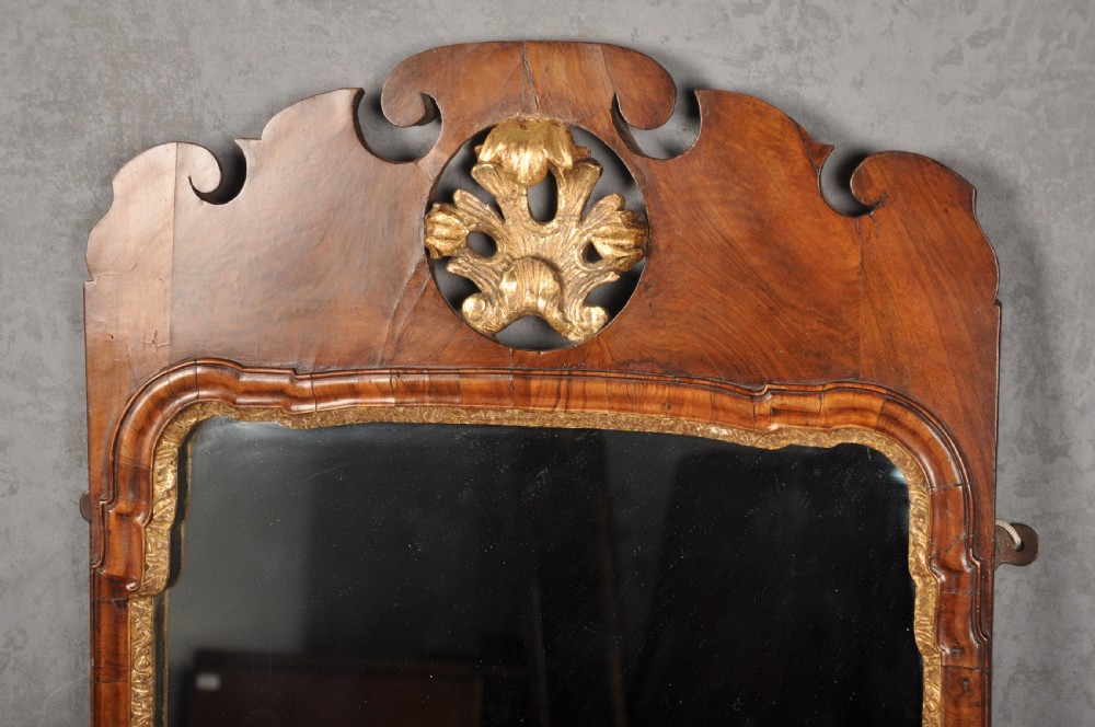 An early 18th-century walnut wall mirror featuring shaped scroll cresting with a carved giltwood shell motif and a gilded inner slip surrounding a rectangular mirror glass. View II