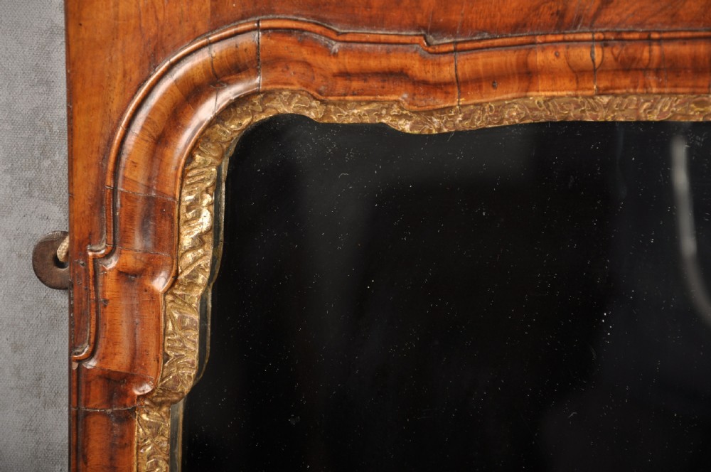 An early 18th-century walnut wall mirror featuring shaped scroll cresting with a carved giltwood shell motif and a gilded inner slip surrounding a rectangular mirror glass. View III