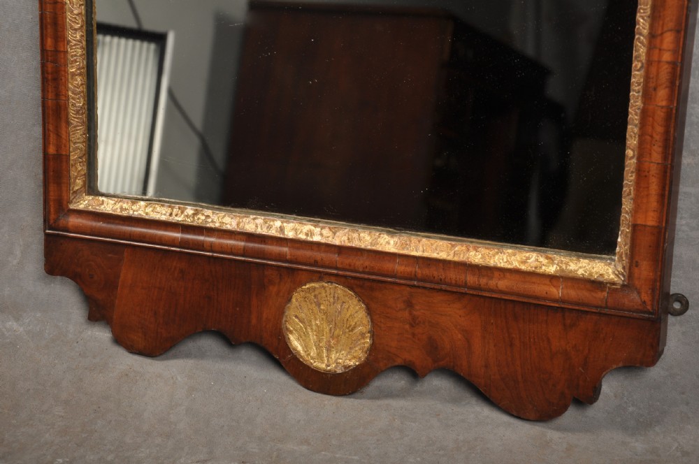 An early 18th-century walnut wall mirror featuring shaped scroll cresting with a carved giltwood shell motif and a gilded inner slip surrounding a rectangular mirror glass. View IV