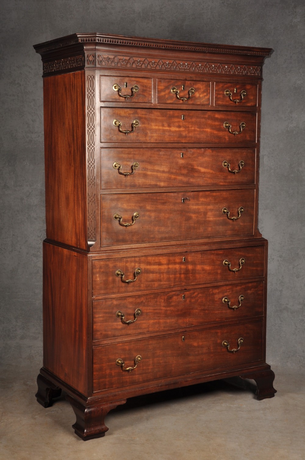 An 18th-century Georgian flame mahogany tallboy featuring a carved fretwork cornice, brass swan-neck handles, and ogee bracket feet.