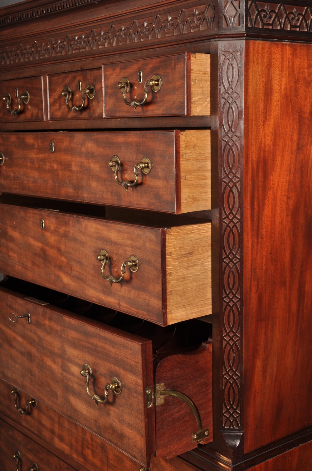 An 18th-century Georgian flame mahogany tallboy featuring a carved fretwork cornice, brass swan-neck handles, and ogee bracket feet. View XIX