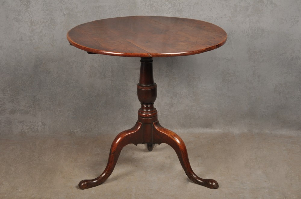 An 18th-century cherrywood tripod table featuring a circular top, turned baluster pedestal, and three splayed cabriole legs.