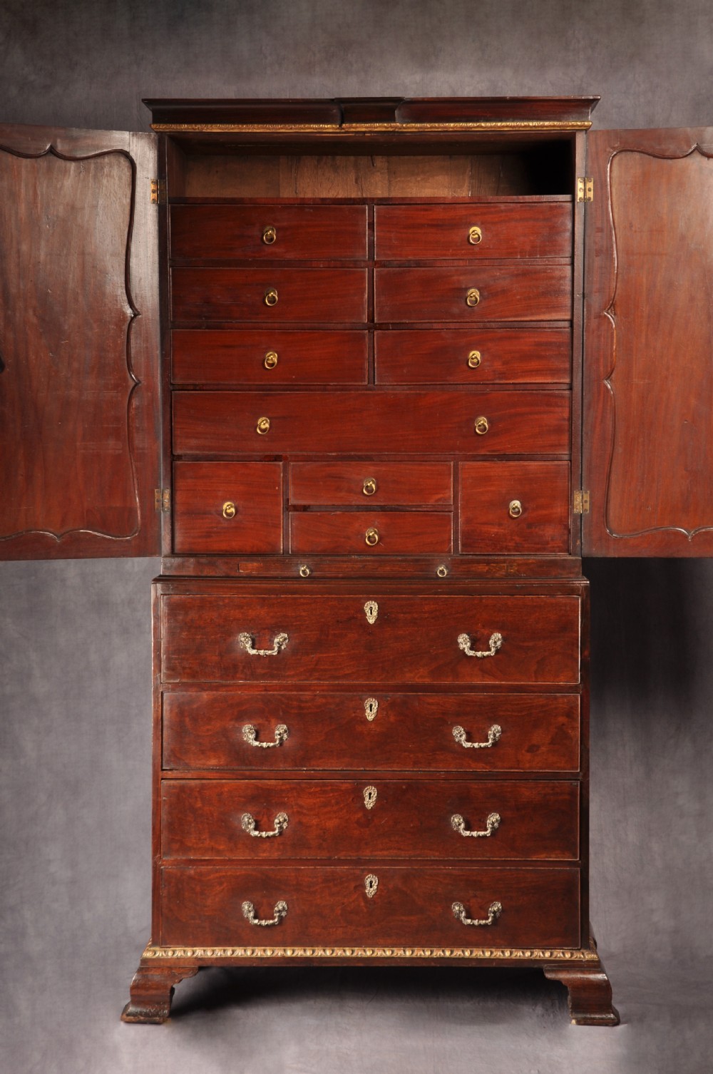 An 18th-century mahogany secretaire cabinet featuring twin upper doors with shaped gilded mouldings above an open fall-front desk with pigeonholes and three drawers on bracket feet. View III