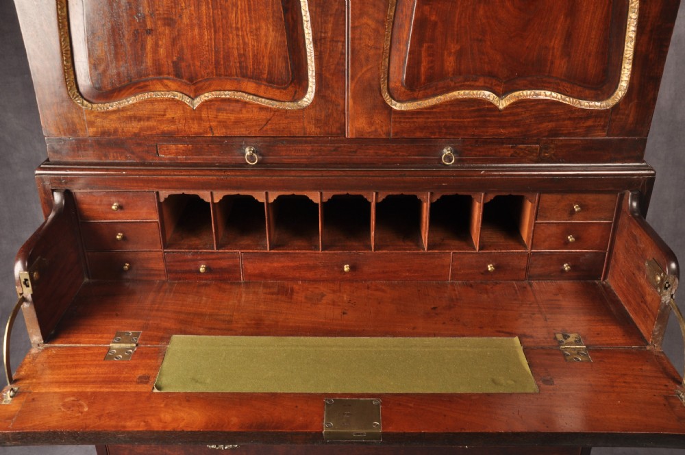An 18th-century mahogany secretaire cabinet featuring twin upper doors with shaped gilded mouldings above an open fall-front desk with pigeonholes and three drawers on bracket feet. View IV