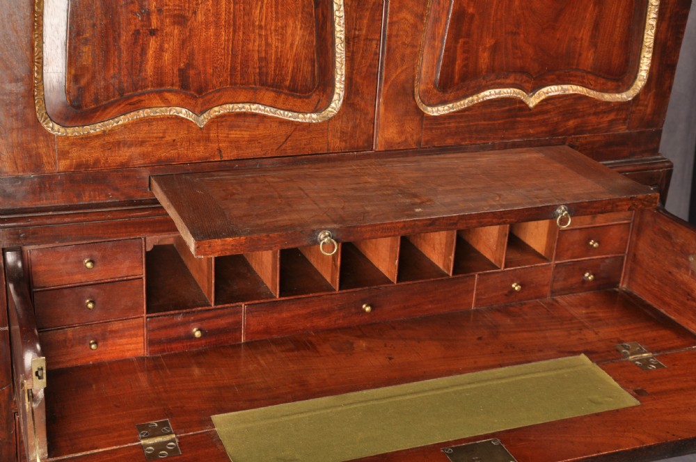An 18th-century mahogany secretaire cabinet featuring twin upper doors with shaped gilded mouldings above an open fall-front desk with pigeonholes and three drawers on bracket feet. View V