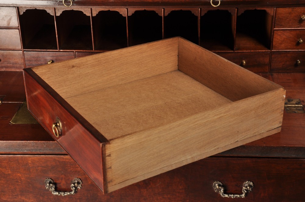 An 18th-century mahogany secretaire cabinet featuring twin upper doors with shaped gilded mouldings above an open fall-front desk with pigeonholes and three drawers on bracket feet. View X