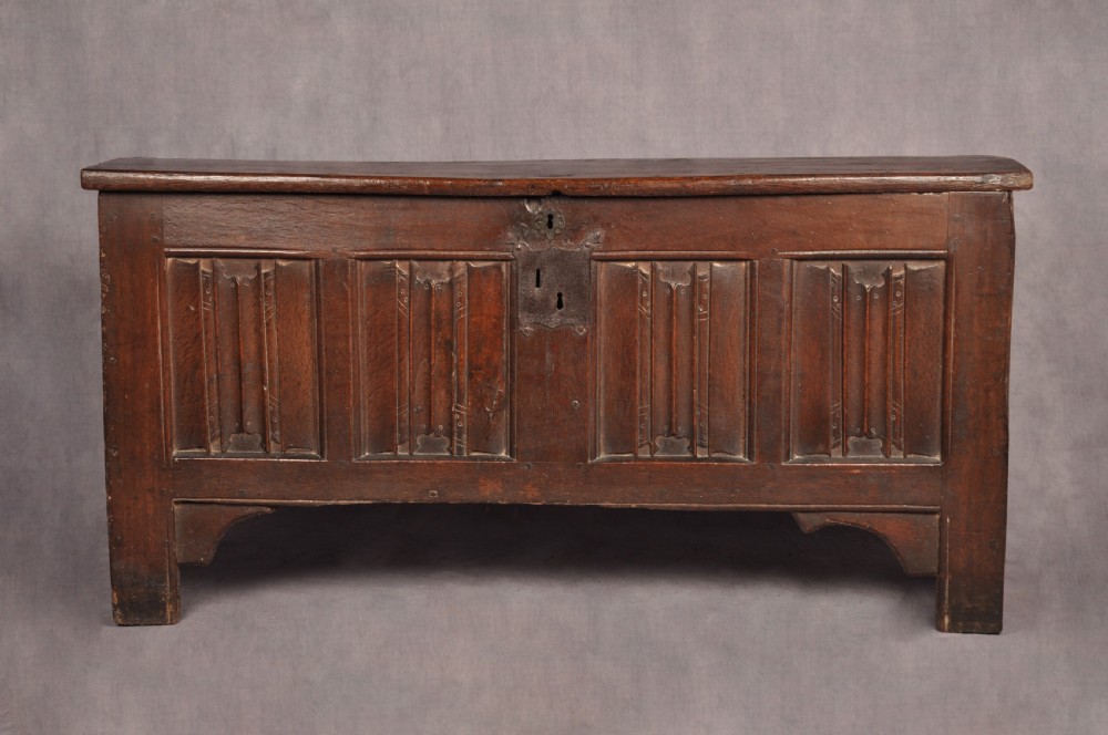 A Tudor era dark oak coffer featuring four carved linenfold panels and an iron lockplate on the front facade.
