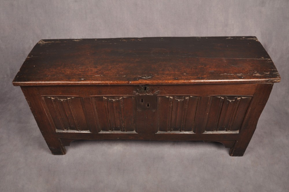 A Tudor era dark oak coffer featuring four carved linenfold panels and an iron lockplate on the front facade. View II