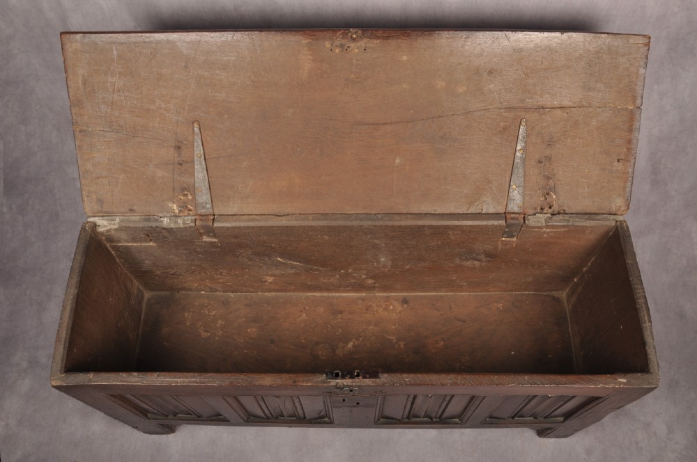 A Tudor era dark oak coffer featuring four carved linenfold panels and an iron lockplate on the front facade. View V