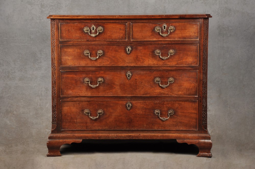 An 18th-century mahogany chest of drawers featuring two short over three long graduated drawers, carved blind fretwork stiles, brass swan-neck handles, and ogee bracket feet.