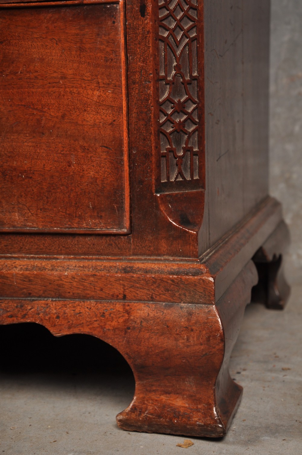 An 18th-century mahogany chest of drawers featuring two short over three long graduated drawers, carved blind fretwork stiles, brass swan-neck handles, and ogee bracket feet. View IV
