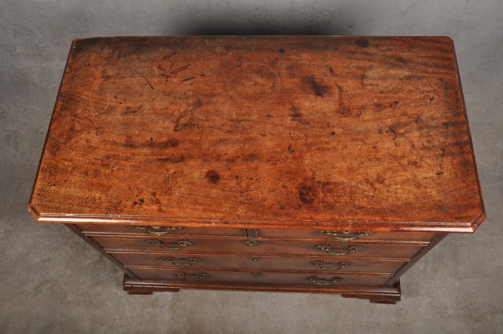 An 18th-century mahogany chest of drawers featuring two short over three long graduated drawers, carved blind fretwork stiles, brass swan-neck handles, and ogee bracket feet. View V