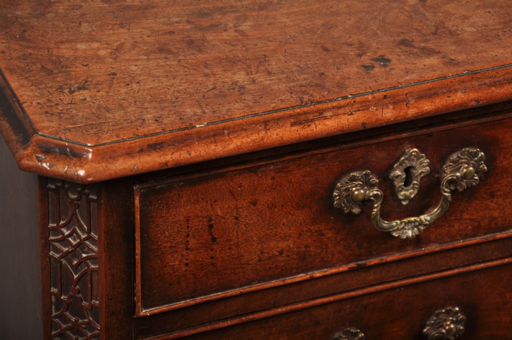 An 18th-century mahogany chest of drawers featuring two short over three long graduated drawers, carved blind fretwork stiles, brass swan-neck handles, and ogee bracket feet. View VI
