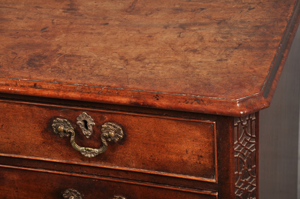 An 18th-century mahogany chest of drawers featuring two short over three long graduated drawers, carved blind fretwork stiles, brass swan-neck handles, and ogee bracket feet. View X