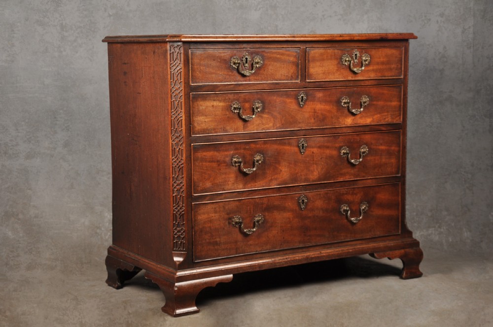 An 18th-century mahogany chest of drawers featuring two short over three long graduated drawers, carved blind fretwork stiles, brass swan-neck handles, and ogee bracket feet. View XIV