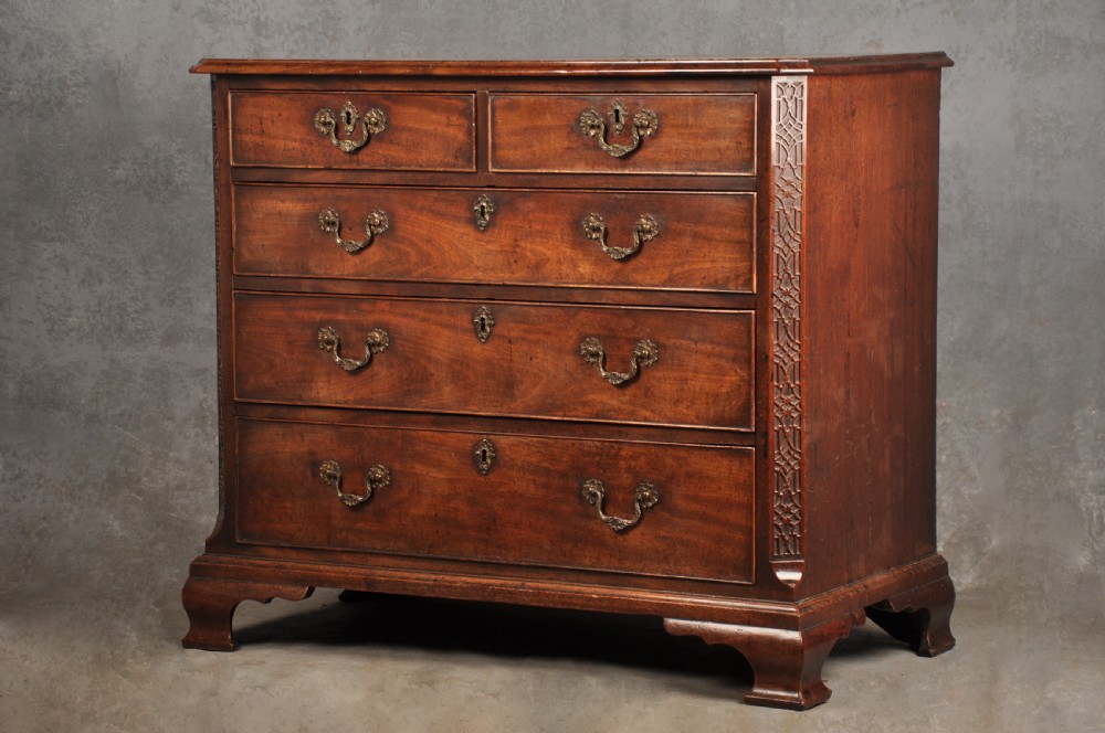 An 18th-century mahogany chest of drawers featuring two short over three long graduated drawers, carved blind fretwork stiles, brass swan-neck handles, and ogee bracket feet. View XV