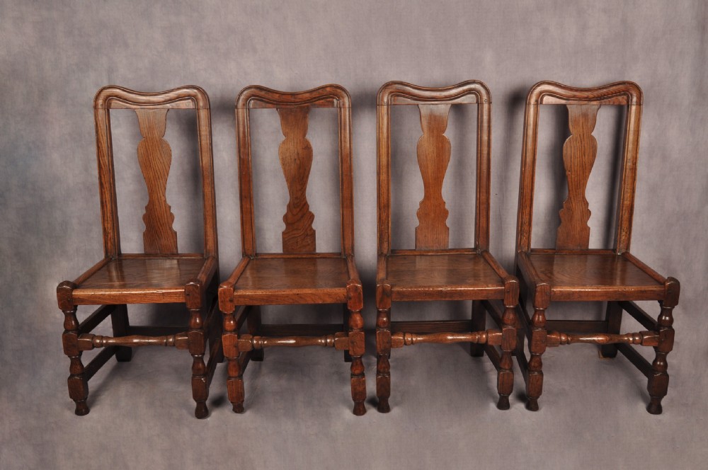 A set of four antique Queen Anne oak and elm side chairs featuring contoured vase backsplats, solid wooden seats, and turned front legs with stretchers.