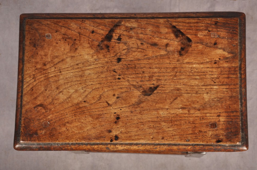 A dark oak joint stool featuring a rectangular moulded top above a carved frieze, supported by turned legs joined by low stretchers. View III