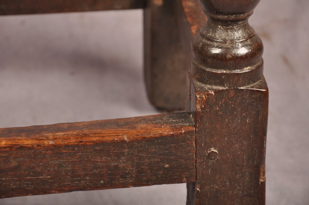 A dark oak joint stool featuring a rectangular moulded top above a carved frieze, supported by turned legs joined by low stretchers. View IX
