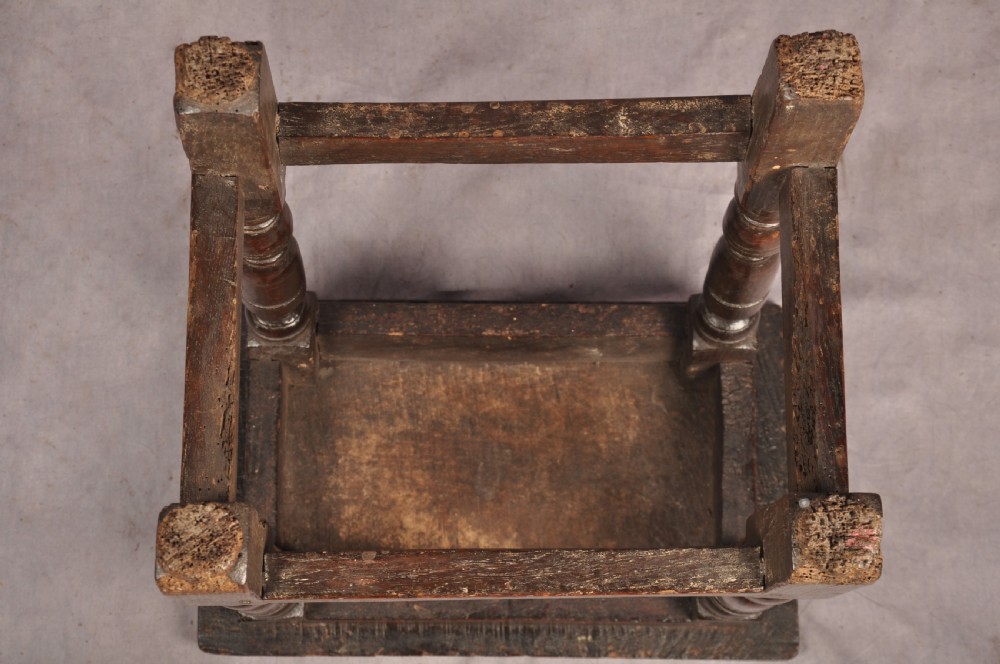 A dark oak joint stool featuring a rectangular moulded top above a carved frieze, supported by turned legs joined by low stretchers. View XII