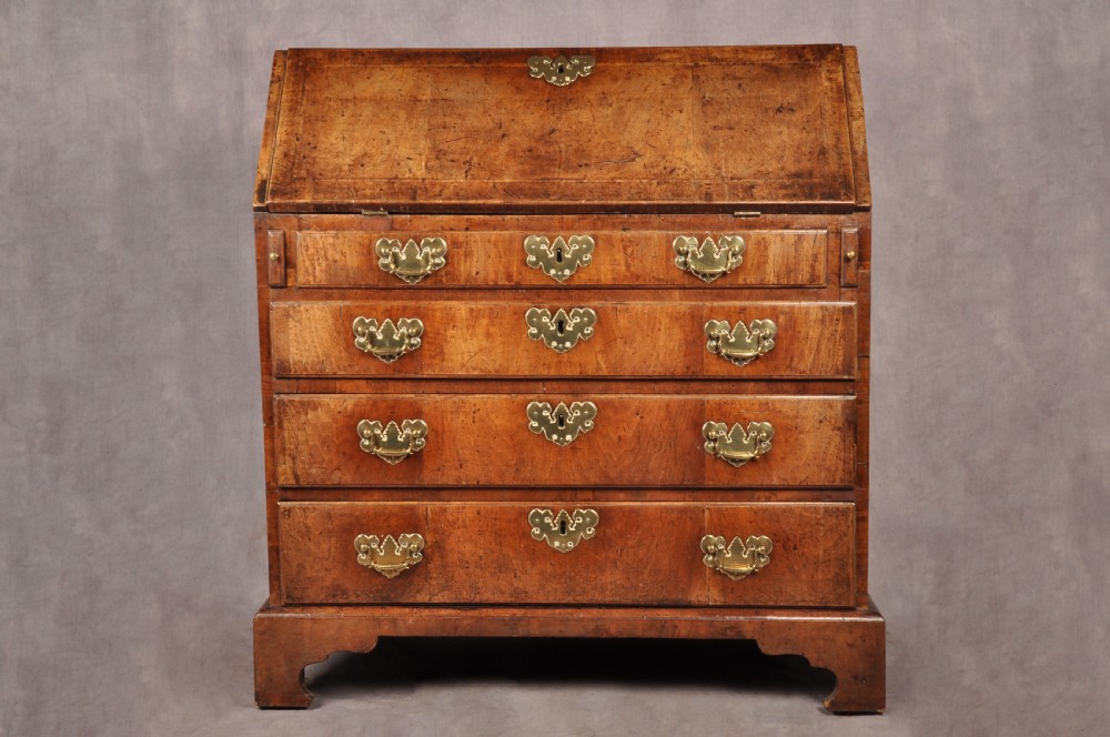 An early eighteenth-century walnut bureau with a sloping fall front, four drawers, decorative brass handles, and bracket feet.