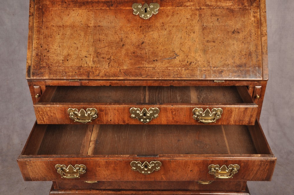 An early eighteenth-century walnut bureau with a sloping fall front, four drawers, decorative brass handles, and bracket feet. View IV
