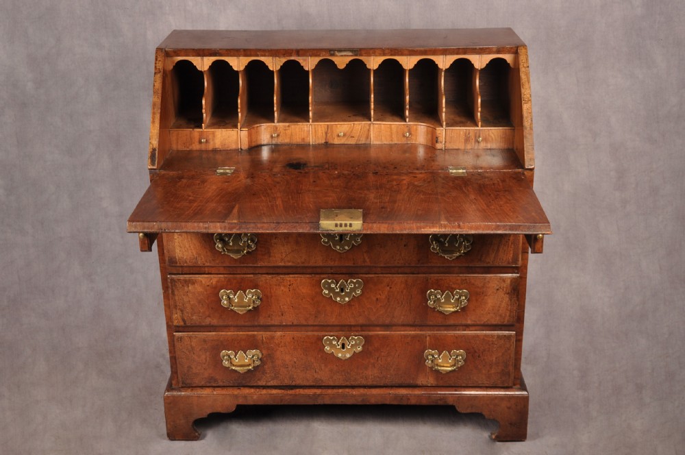 An early eighteenth-century walnut bureau with a sloping fall front, four drawers, decorative brass handles, and bracket feet. View V