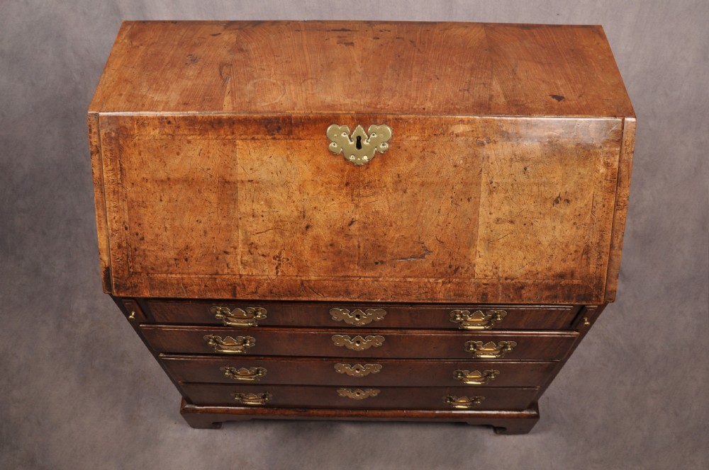 An early eighteenth-century walnut bureau with a sloping fall front, four drawers, decorative brass handles, and bracket feet. View XI