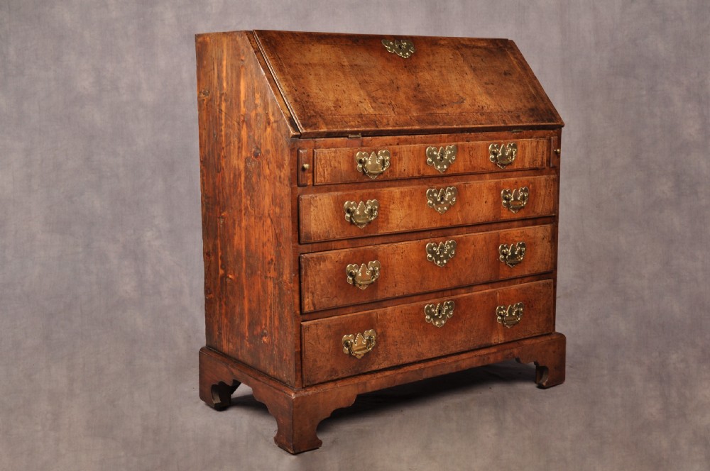 An early eighteenth-century walnut bureau with a sloping fall front, four drawers, decorative brass handles, and bracket feet. View XII