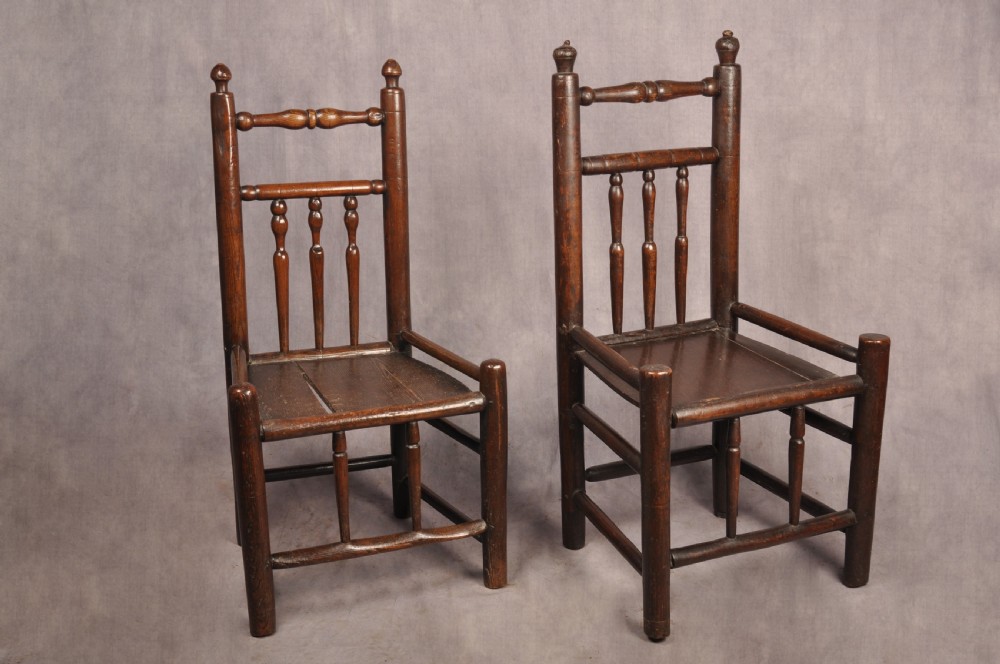 A near pair of dark 17th-century turned ash chairs with spindle backrests, turned stretchers, panel seats, and top finials.
