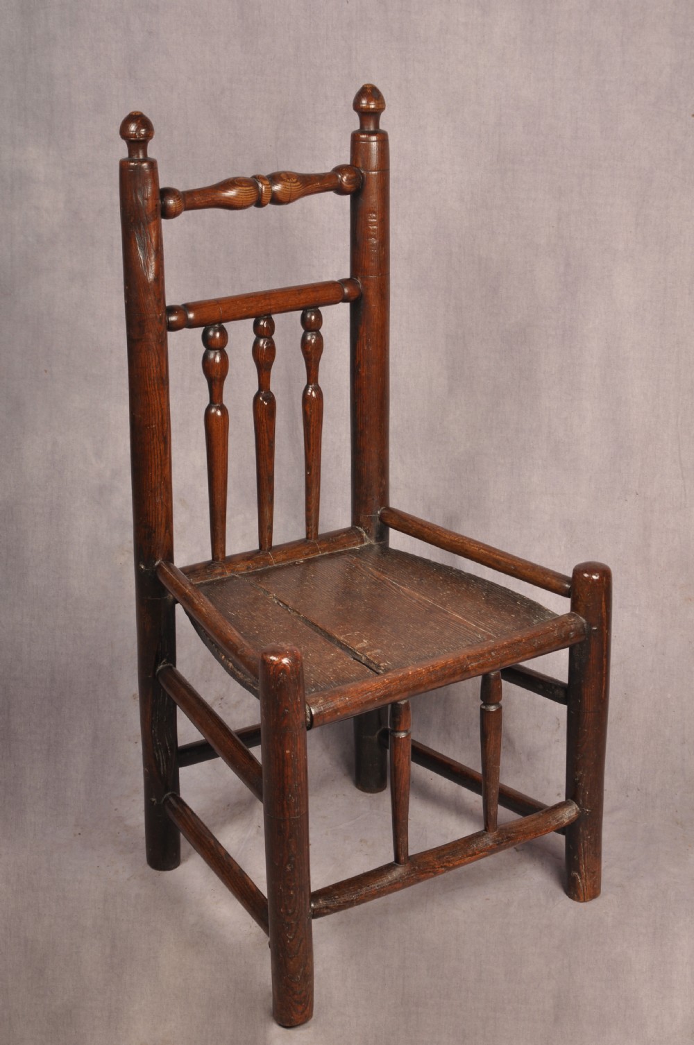 A near pair of dark 17th-century turned ash chairs with spindle backrests, turned stretchers, panel seats, and top finials. View II